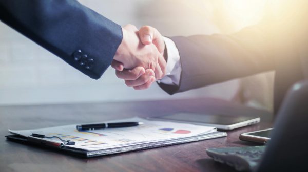 Two business professionals shaking hands across a desk after reaching a successful business agreement.